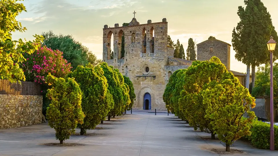 Old stone church with walk with trees at sunset in the town of Peratallada, Girona, Spain.